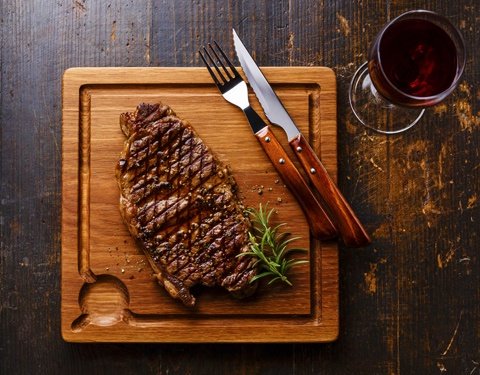 Grilled striploin steak served on wooden cutting board paired with glass of red wine