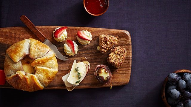 Wooden cheese board, brie in pastry, jam, grapes