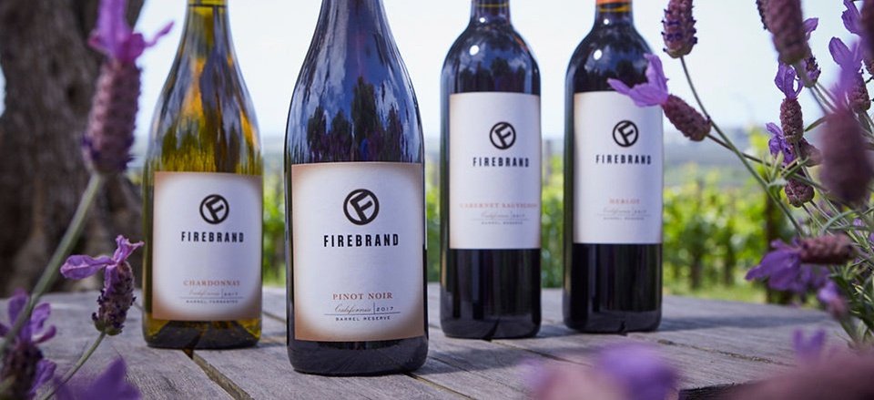 Bottles of Firebrand Chardonnay, Pinot Noir, Cabernet Sauvignon and Merlot on a picnic table surrounded by lavender plants