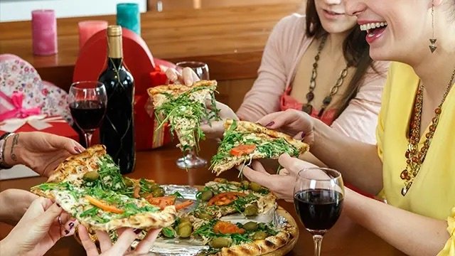 Four women eating pizza, red wine
