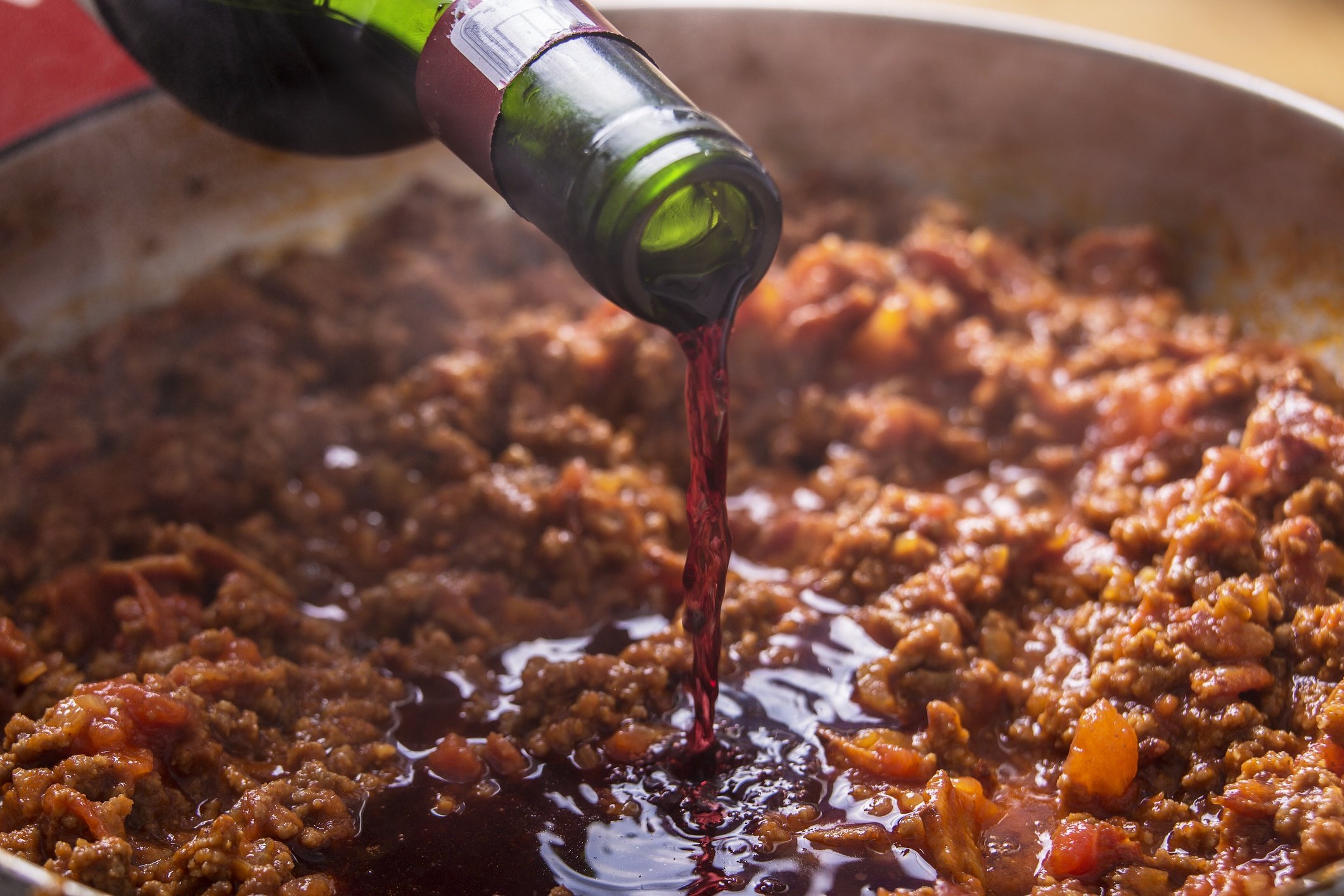 pouring red wine into meat sauce